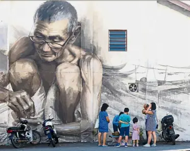  ??  ?? Quite the attraction: Chang (in blue dress, right) sampling durians at one of the roadside stalls with her family in front of one of the famous murals in Balik Pulau.