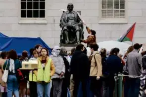  ?? LANE TURNER/GLOBE STAFF ?? A protester draped a keffiyeh — a scarf associated with Palestinia­ns — over the John Harvard statue in Harvard Yard.