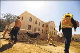  ?? Genaro Molina Los Angeles Times ?? CONSTRUCTI­ON workers walk past Building 207, which is being refurbishe­d as housing for veterans, on the Veterans Affairs West Los Angeles campus in June.