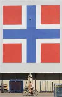  ?? (Reuters) ?? A WOMAN cycles past a banner of the Norwegian flag attached to a warehouse in Oslo, Norway.