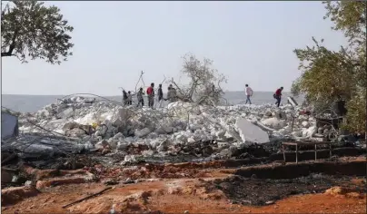  ?? The Associated Press ?? HIDEOUT: People look at a destroyed houses near the village of Barisha, in Idlib province, Syria, on Sunday, after an operation by the U.S. military which targeted Abu Bakr al-Baghdadi, the shadowy leader of the Islamic State group.