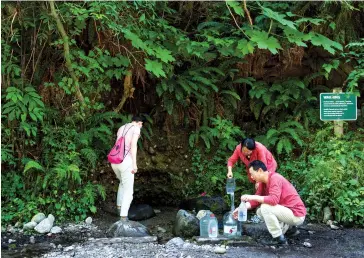  ??  ?? Min Wu (centre) and two other people draw spring water near Lynn Headwaters Regional Park