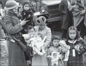  ?? FILE — THE ASSOCIATED PRESS ?? Cpl. George Bushy, left, a member of the military guard which supervised the departure of 237 Japanese people for California, holds the youngest child of Shigeho Kitamoto, center, as she and her children are evacuated from Bainbridge Island, Wash., in 1942.