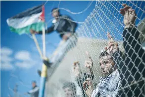  ??  ?? PALESTINIA­NS STAND behind a fence as they wait for the arrival of their relatives at Rafah crossing after it was opened by Egyptian authoritie­s over the weekend.