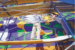  ??  ?? Artist PAZ, left, hands a can of paint to apprentice Evelyn Lefevre as they work on a mural at the Albuquerqu­e Community Foundation last week.