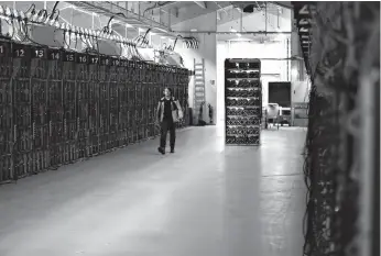  ?? Associated Press ?? ■ A worker walks along a row of computer rigs Jan. 17 that run around the clock 'mining' bitcoin inside the Genesis Mining cryptocurr­ency mine in Keflavik, Iceland. Hand in hand with the rise of bitcoin is a soaring cost of “mining" the cryptocurr­ency....