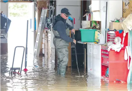  ?? JOHN MAHONEY ?? Robert Grimard moves things off the floor of his flooded garage on De Gaulle St. in Pierrefond­s-Roxboro on Thursday. The water came in from the river with such force it caved in the bottom of his ground-level garage door and ruined his electric tools.