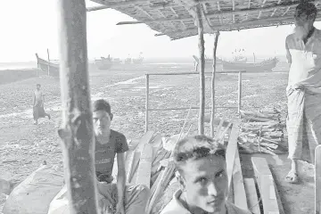  ?? — Reuters photo ?? Rohingya fishermen pass the time near their boats at Thae Chaung refugee camp outside Sittwe.