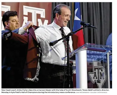  ?? DAVE MCDERMAND / COLLEGE STATION EAGLE ?? New head coach Jimbo Fisher slips into a maroon blazer with the help of Scott Woodward, Texas A&M’s athletic director, Monday in Kyle Field’s Hall of Champions during the introducto­ry news conference.