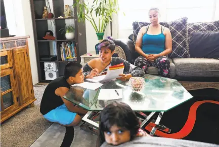  ?? Photos by Gabrielle Lurie / The Chronicle ?? Briza Moreno, 19 (center), helps her brother Gael Ayala, 7, at home with mom Miriam Moreno and sister Kimberly Ayala, 6.