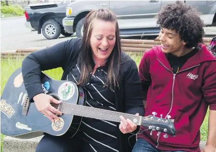  ??  ?? Family friend Jen Macpherson strums a guitar with Wade Saint-Ange outside the Saint-Ange home. The family hopes a gofundme campaign will allow them to stay together until everyone is finished school.