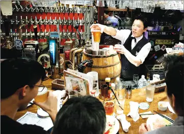  ?? — WP-Bloomberg photo by Kiyoshi Ota ?? A bartender serves a glass of craft beer to a customer inside the Bakusyu Club Popeye bar in the Ryogoku neighbourh­ood of Tokyo.