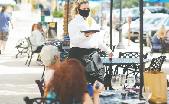  ?? Zack Wittman / Bloomb erg ?? A server wearing a protective mask serves a drink to a customer in the outside dining area of a restaurant in St. Petersburg, Fla.,
on Monday as the state, along with Georgia and Texas, went furthest in the U. S. on allowing businesses to reopen.