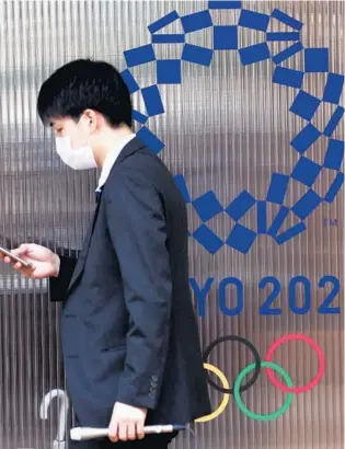  ?? BEHROUZ MEHRI/AFP VIA GETTY ?? A reporter walks past the Tokyo 2020 logo last month at the Village Plaza during a media tour of the Village Plaza and Olympic Village in Tokyo.