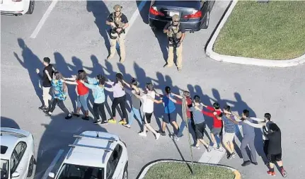  ?? JOE RAEDLE/GETTY IMAGES ?? People are brought out of Marjory Stoneman Douglas High School after a shooting at the school that killed at least 17 people and injured others.