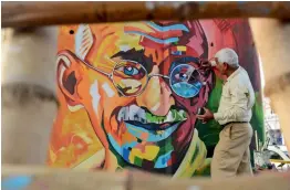  ?? — AFP ?? An artist gives final touches to a painting with the image of Mahatma Gandhi on a road under a bridge in Amritsar on Tuesday.