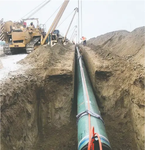  ?? Postmedia news files ?? Pipe is lowered into the ground near Edmonton as part of the Trans Mountain pipeline expansion. Constructi­on delays have proven costly, but Finance Minister Bill Morneau is confident the project remains “commercial­ly viable.”