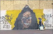  ??  ?? A woman carrying a shopping bag walks by Black Lives Matter artwork posted on wooden panels that barricade shops because of on-going protests in downtown Portland, Ore., on June 5.