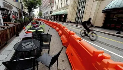  ?? Darrell Sapp/Post-Gazette ?? A cyclist goes past a set of orange barriers enclosing chairs and tables that will be used for dining along Sixth Street between Liberty and Penn avenues Monday in Downtown.