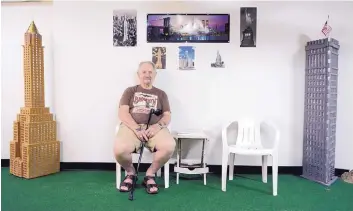  ?? GREG SORBER/JOURNAL ?? Bill Falkenthal sits in his basement between two of his NYC landmark creations. To his left is the Chrysler Building and to the right is the iconic Flat Iron Building.