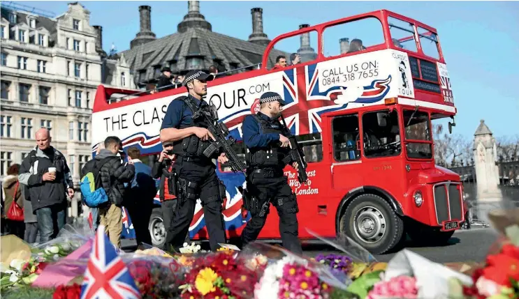  ??  ?? Armed police officers pass tributes to the victims of the Westminste­r attack in Parliament Square yesterday.
