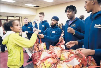  ?? STEPHEN DUNN/SPECIAL TO THE COURANT ?? Keisha Morgan of Hartford, left, accepts her bag of groceries from Delshawn Jackson Jr., third from left, a member of the St. Joseph team and Prince Tech alumn. From left to right are St. Joseph teammates Brad Landry, Ryan O’Neill, Jackson, Tyree Mitchell, also from Prince Tech, and Alec Kinder.