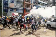  ?? (AP) ?? Anti-coup protesters run as one of them discharges a fire extinguish­er to counter the impact of tear gas fired by riot police Wednesday in Rangoon, Burma.