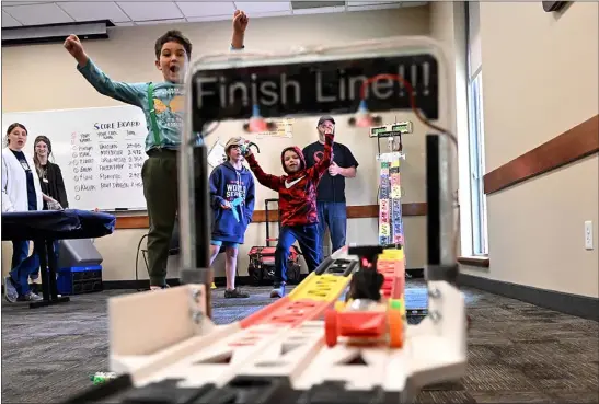  ?? JENNY SPARKS — LOVELAND REPORTER-HERALD ?? Kalvin Lawrence, 6, left, Ealan Backo, 9, center left, and Elwood Griesel, 6, cheer as they compete with the gravity racers they built Friday on a 3D printed racetrack during the Nerdy Derby event at the Loveland Public Library in Loveland. Brian Cleveland, a board member at Creatorspa­ce Loveland, right, runs the track.