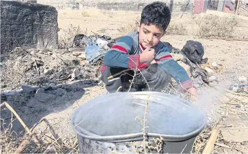  ??  ?? WAITING IN VAIN: Ubaida, six, heats water over an outdoor fire in Fallujah, Iraq. His father moved them back to their ransacked home but the family waits in frustratio­n for promised aid.