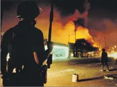  ?? Gary Friedman Los Angeles Times ?? AN LAPD officer guards the intersecti­on of Central Avenue and 46th Street on April 30, 1992. Police stood idly by as neighborho­ods burned.