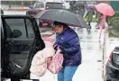  ?? MARCIO JOSE SANCHEZ/AP ?? A safety supervisor helps a child out of a car during a rainstorm Friday outside a school in Newhall, Calif. California and other parts of the West faced snow and rain Friday from the latest winter storm to pound the U.S.