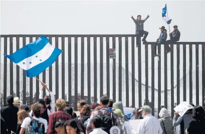  ?? CHRIS CARLSON/THE ASSOCIATED PRESS ?? Central American migrants sit on top of the border wall on the beach in San Diego during a gathering of migrants along the border.