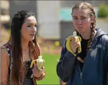  ??  ?? Jordan Creamer, a junior from Pittman, and Emily Burkhart, a sophomore from Hershey, enjoy bananas during West Chester University’s “Banana Day” a 22-year running rite of spring on campus.