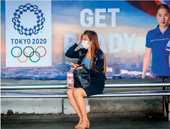  ?? AFP ?? A woman wearing a facemask, amid concerns over the spread of coronaviru­s, sits at a bus stop in front of a Tokyo 2020 Olympics advertisem­ent in Bangkok, Thailand, on Monday. —