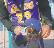  ??  ?? Eric Alcocer puts a mask on daughter, Amari, 3, while waiting in line to enter Adventure City.