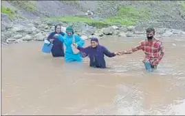  ?? ANI ?? Healthcare worker cross a swollen rivulet with their vaccinatio­n kits at Kandi in Rajouri on Tuesday.