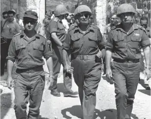  ?? (Ilan Bruner/GPO) ?? THEN-DEFENSE MINISTER Moshe Dayan (center), then-IDF chief of staff Yitzhak Rabin (right) and then-OC Central Command Uzi Narkiss walk through Lions’ Gate into Jerusalem’s Old City in June 1967 during the Six Day War. Dayan demanded the Israeli flag at the Temple Mount be lowered.