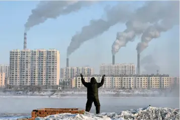  ?? — Reuters ?? A man exercises in the morning as he faces chimneys emitting smoke behind buildings across the Songhua River in Jilin, China, in this file photo.