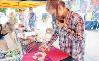  ?? FOTO: LENA REINER ?? Lena arbeitet konzentrie­rt an ihrem T-Shirt und ignoriert Daniel Schweizers fachliche Farbtipps – mit Erfolg: Die grüne Farbe kommt besser zur Geltung als erwartet. Wie viele Jugendlich­e ist sie nicht zum ersten Mal bei dieser Aktion dabei. „Die...