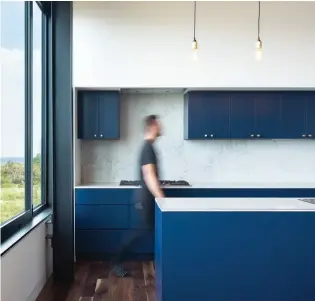  ??  ?? BELOW: Deep-blue cabinetry in the kitchen reflects the house’s seaside setting. A row of single-bulb ceiling lights hangs over the central island.