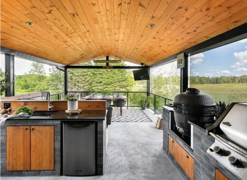  ??  ?? Popoter à l'intérieur ou à l'extérieur ? Ce genre de dilemme n'a pas sa place ici, puisque cette terrasse accolée à la maison dispose d'une cuisine équipée de tout ce qu'il faut pour faire le bonheur du chef cuistot, barbecue et fumoir compris. Le gris (sol en béton), le bois de pin et le noir (comptoirs en granit, éléments structurel­s) unifient les espaces.