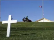  ?? ASSOCIATED PRESS ?? A cross marks the grave of Robert F. Kennedy as a groundskee­per mows the grass near the Arlington House, right, at Arlington National Cemetery in Arlington, Va.