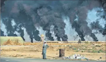  ?? AFP/FILE ?? A woman stands along the side of a road near the Syrian town of Tal Tamr in Hassakeh province, with smoke from burning tyres billowing in the background. The entire country, most recently Idlib province, has been ravaged by conflict and war for nearly a decade.