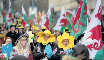  ??  ?? > People carry Welsh flags as they attend the St David’s Day parade in Cardiff