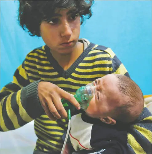  ?? HASAN MOHAMED / AFP VIA GETTY IMAGES ?? A Syrian boy holds an oxygen mask over the face of an infant at a makeshift hospital following a reported gas attack
on the besieged town of Douma, in the eastern Ghouta region, on the outskirts of Damascus in 2018.