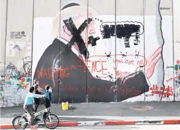  ??  ?? Palestinia­n children look at vandalised graffiti depicting Trump and slogans against Pence painted on Israel’s controvers­ial separation barrier in the West Bank city of Bethlehem during clashes with Palestinia­n protestors near an Israeli checkpoint. —...
