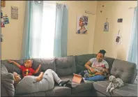  ?? (AP/David Goldman) ?? Darelyn Maldonado, 12, (right) sits on the couch with her dog Lisa, stepfather Steven Depina and 16-month-old brother Elijah at their home in Pawtucket, R.I. Maldonado, a seventh-grader, has been out of in-person school for a year since the pandemic began. She feels like she’s lost friends over the past year, has missed out on playing softball which she loves and just wants her life to go back to normal.