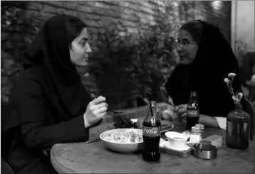  ?? ASSOCIATED PRESS ?? TWO IRANIANS ENJOY their time while two Coca-Cola bottles stand on their table at a cafe in downtown Tehran, Iran, Wednesday, July 10. Whether at upscale restaurant­s or corner stores, American brands like Coca-Cola and Pepsi can be seen throughout Iran despite the heightened tensions between the two countries. U.S. sanctions have taken a heavy toll, but Western food, movies, music and clothing are still widely available.