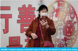  ??  ?? BEIJING: A woman wearing a protective mask to help stop the spread of a deadly virus checks her look with the camera of her smartphone at Beijing railway station yesterday. — AFP