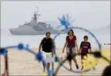  ?? SILVIA IZQUIERDO — THE ASSOCIATED PRESS FILE ?? In this file photo, a family walks on the shore of Copacabana beach backdroppe­d by a Brazilian navy vessel, in Rio de Janeiro, Brazil. There are expected to be 85,000 military personnel and police fanning out across the city, double the number that was...